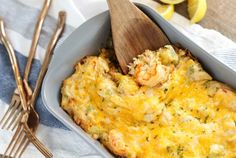 a casserole with shrimp and cheese in a blue dish next to silverware