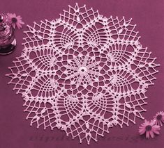 a crocheted doily sits on a purple surface next to some daisies