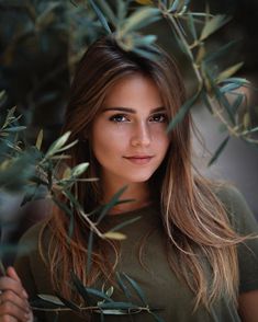 a beautiful young woman standing next to an olive tree