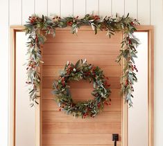 a wooden door decorated with christmas wreaths and greenery hanging on the side wall