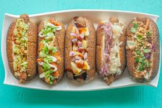 four hot dogs with different toppings are on a white platter against a turquoise background