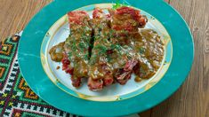 two pieces of meat covered in gravy on a blue and yellow plate next to a wooden table