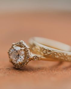 two gold wedding rings sitting on top of a wooden table next to another ring with a diamond