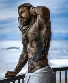 a man with tattoos on his back standing next to a railing looking at the ocean