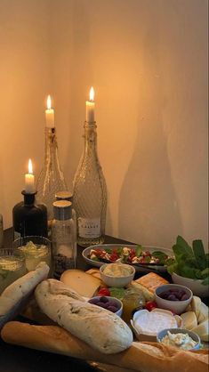 a table topped with lots of food next to two lit candles and bottles filled with wine