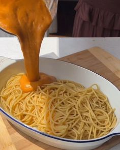 someone is pouring sauce over spaghetti in a bowl