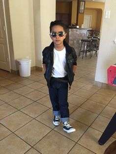 a young boy wearing sunglasses and standing on the floor in front of a tile floor