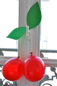 two red balloons hanging from the side of a window with green leaves on top of them