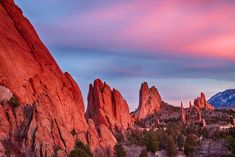 the sun is setting over some rocks and trees in front of mountains with snow on them