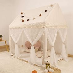 a white tent with curtains and teddy bears on the floor next to it in a room