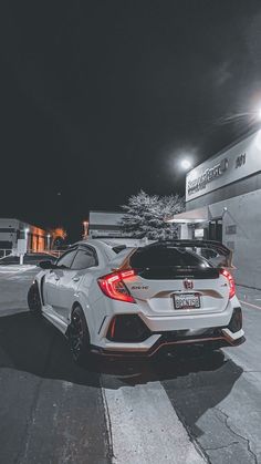 two white cars parked in front of a building on a street at night with the lights on