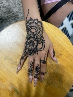 a woman's hand with henna tattoos on her left and right palm, sitting on a wooden table