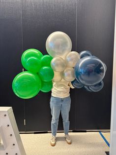 a person standing in front of a black wall holding up some green and white balloons