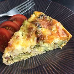 a piece of quiche on a plate with tomatoes and a fork next to it