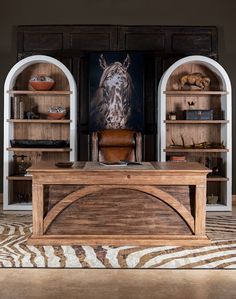 a wooden desk sitting in the middle of a living room next to two bookshelves