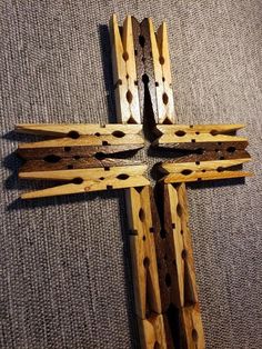 a wooden cross with holes in the middle on a gray carpeted floor, next to a piece of wood that has been cut into smaller pieces