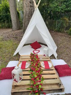 a teepee tent set up with red and white pillows, napkins and plates