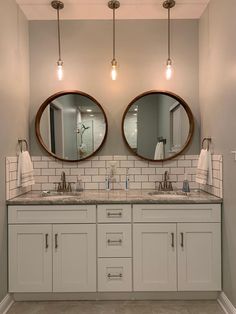 two round mirrors are above the double sink vanity in this modern bathroom with white cabinets and marble countertops