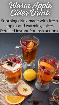 two glasses filled with apple cider drink next to sliced oranges and an apple