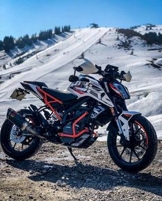 a white and red motorcycle parked on top of a snow covered mountain next to trees