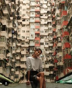 a woman sitting on the edge of a wall in front of a building with many balconies