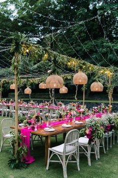 an outdoor dining area with tables and chairs covered in pink tablecloths, hanging lights and greenery