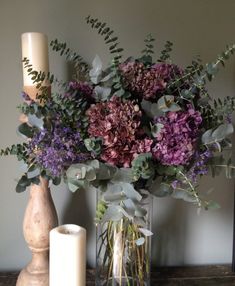 a vase filled with lots of purple flowers next to a candle and some greenery