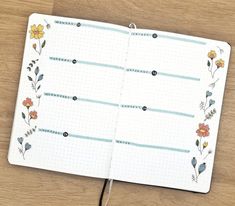 an open notebook with flowers on it sitting on a wooden table next to a pen