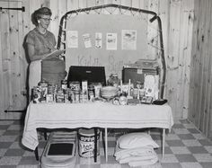 an old black and white photo of a woman standing in front of a table full of food