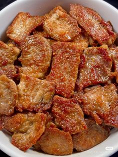 a white bowl filled with cooked meat on top of a table