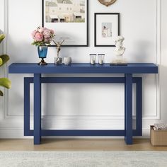 a blue console table with vases and flowers on it in front of a white wall