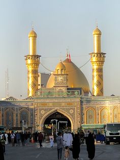 several people are walking around in front of a large building with gold domes and arches