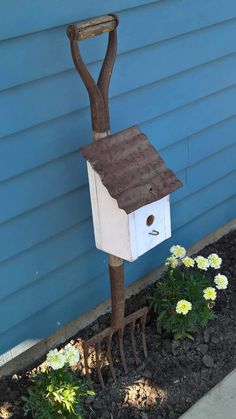 a bird house made out of tree branches and some flowers in front of a blue building