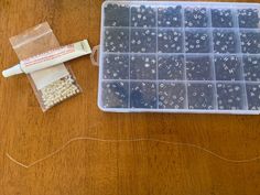 a plastic container filled with lots of beads next to a string on a wooden table