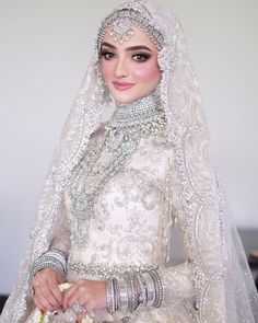 a woman in a white wedding dress and veil with jewelry on her head, holding a bouquet