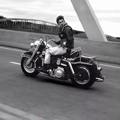 a man riding on the back of a motorcycle down a street next to a bridge