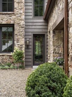 a stone house with two windows and some bushes in front of the door is shown