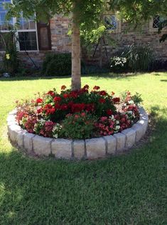 a flower bed in front of a brick house with trees and flowers around it on the lawn