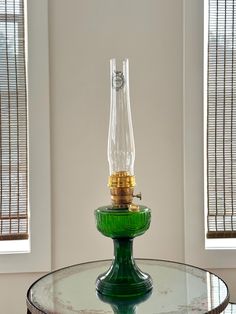 a green glass table with a light on top and two windows behind it in the background