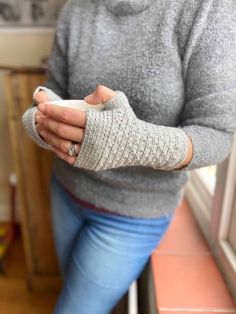 a woman with her arm wrapped in a knitted mitt sitting on a window sill