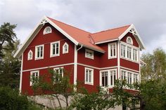 a red house with white trim on the roof and windows is surrounded by greenery