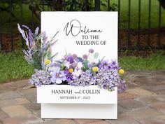 a wedding sign with flowers on it sitting in front of a brick walkway and gate