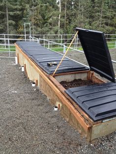 an open box sitting on top of a gravel ground next to a fence and trees