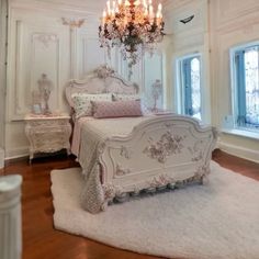 a white bedroom with chandelier, bed and rug on the floor in front of two windows