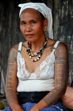 an old woman with tattoos on her arms and chest sitting in front of a wooden wall