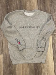 Adult crewneck sweatshirt 50/50 poly/cotton with "I WEAR MY HEART ON MY SLEEVE" across chest area in iron on. Child/Children's names on sleeve with RED heart in iron on. A personalization specialist will contact you within 1-2 business days after placing your order with your names and order for approval. THIS ITEM GETS FREE ECONOMY SHIPPING! Care instructions - For best results wash inside out in cold water and tumble dry low. Wear My Heart On My Sleeve Shirt, I Wear My Heart On My Sleeve, I Wear My Heart On My Sleeve Sweater, Iron On Sweatshirt Ideas, Heart On My Sleeve Shirt, Cricut Sweatshirt, Cricut Sweatshirt Ideas, Cold Hands Warm Heart, Heart On My Sleeve