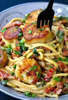 a fork is stuck into some pasta with scallops