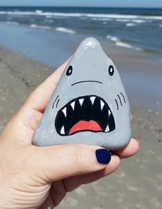 a hand holding up a rock with a shark face painted on it's side