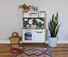 a toy kitchen with a potted plant next to it and a rug on the floor