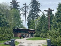 two people walking down a dirt road in front of tall trees and a building with a cross on it